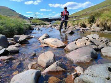 Man standing in a low river Tweed measuring the flow