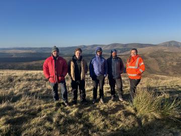 Five colleagues stand in the Tweed catchment, with a hilly backdrop behind them