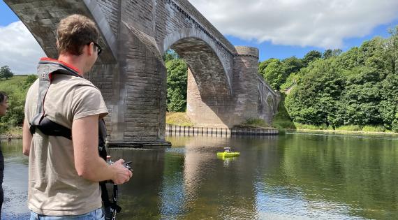 Man with controls for arc boat on a river, with bridge in background