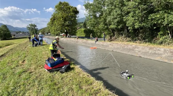 A woman stands on the canal bank with a Hydroboard attached to string in the water