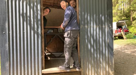 Three men cut a ribbon in front of a metal hut