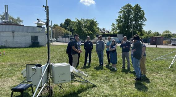 A group stands behind scientific monitoring equipment under a blue sky