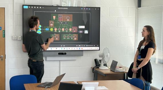 A man stands in front of a flow diagram on a large tv screen