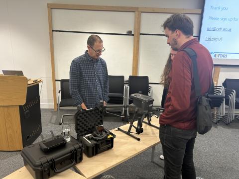 Two scientists discuss the drones and other sensing equipment on display on the table