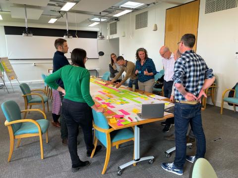 A group of people stand over a table covered in post-its during a planning workshop