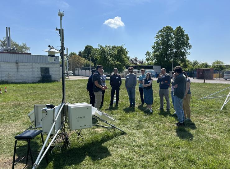 A group stands behind scientific monitoring equipment under a blue sky