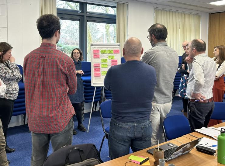 Colleagues stand around a flipchart, brainstorming ideas using post-it notes