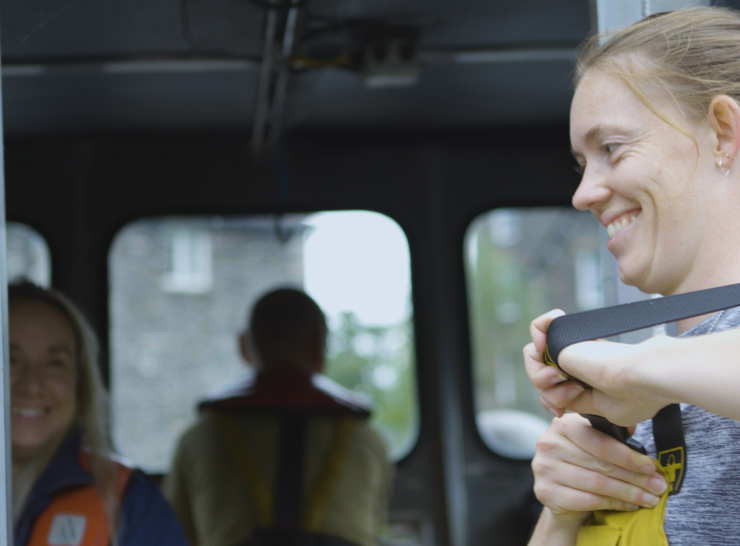 Team member adjusts protective clothing and laughs with colleague on boat