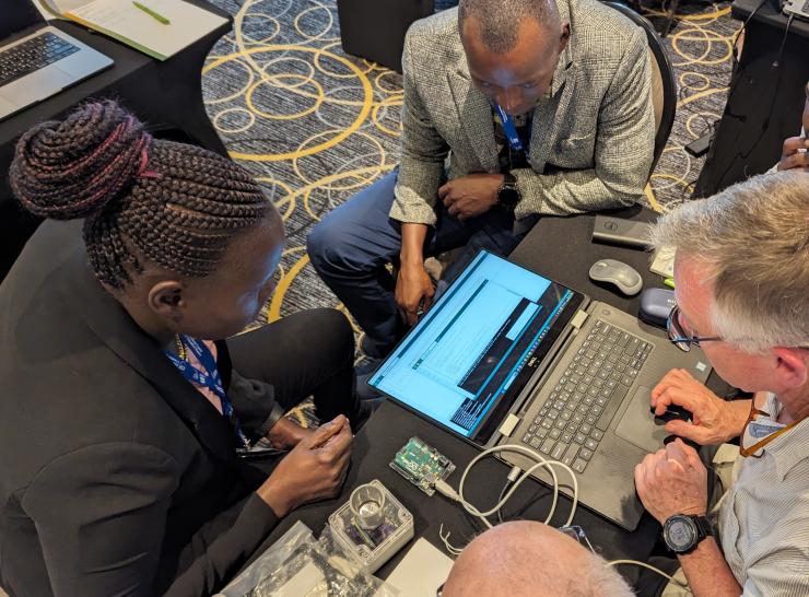 Four individuals gathered around a computer, working with some open hardware