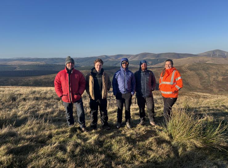Five colleagues stand in the Tweed catchment, with a hilly backdrop behind them