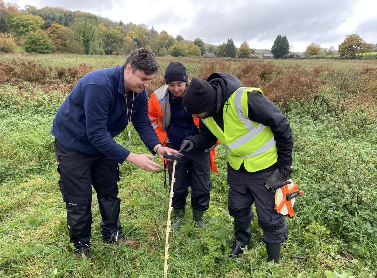 Three field technicians observe measurements in a water meadow